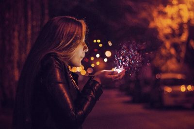 Image - Woman standing in a street at night blowing glowing glitter dust from her hand - Wide-Eyed-Wonder - How We Work Wonders - Children's Entertainment